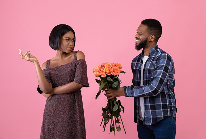 A man tries to give flowers to a woman while she is scowling at him.