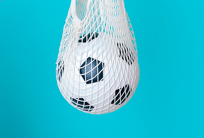 A soccer ball hangs in a white net against a blue background.