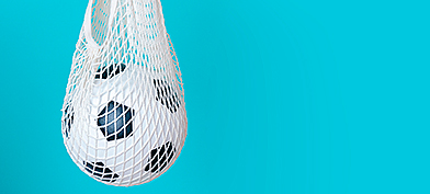 A soccer ball hangs in a white net against a blue background.