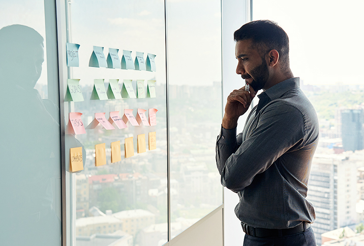 A man stares at a collection of post-it notes placed on a wall at work.
