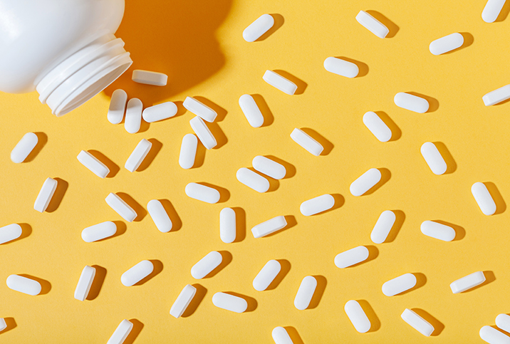 White zinc pills are spread out against a yellow surface with a pill bottle in the corner.