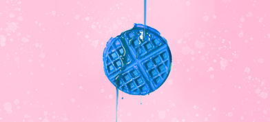 A blue waffle is against a pink background with blue syrup pouring down over it.
