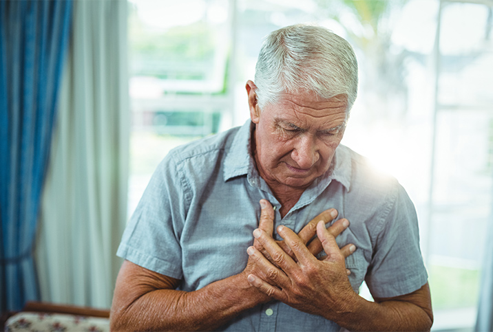 An elderly man with white hair clutches his chest and looks downward.