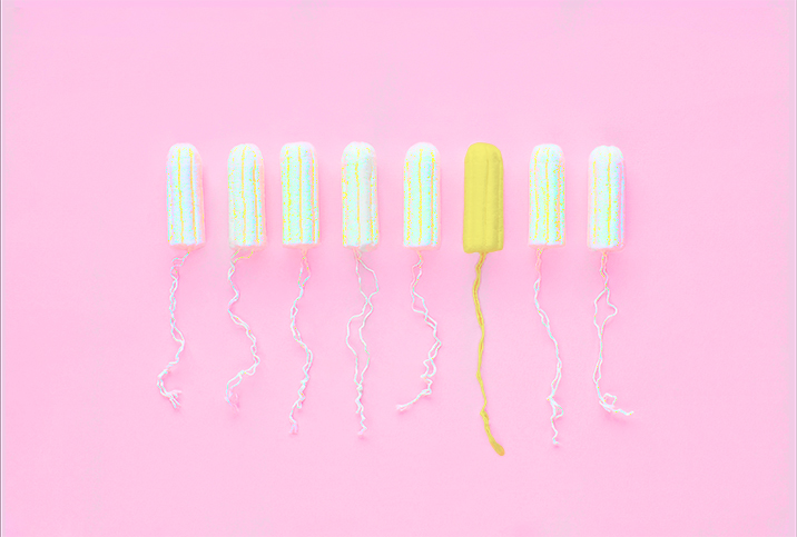 Eight tampons outside of their applicator sit in a row against a pink background and one is yellow.