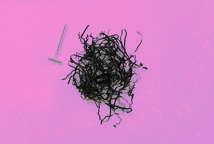 A pile of shredded black paper and a razor sit side by side on a pink background.