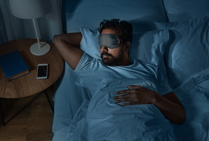 A man sleeps in bed with a facemask on.
