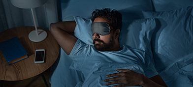A man sleeps in bed with a facemask on.