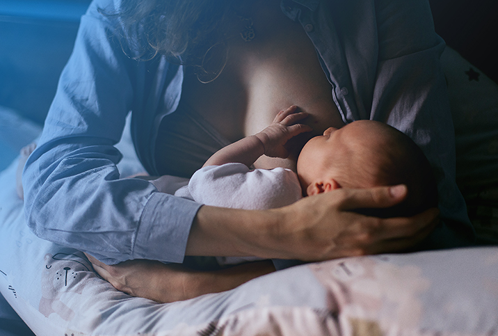 A mother breastfeeds her baby as it lays on a nursing pillow.