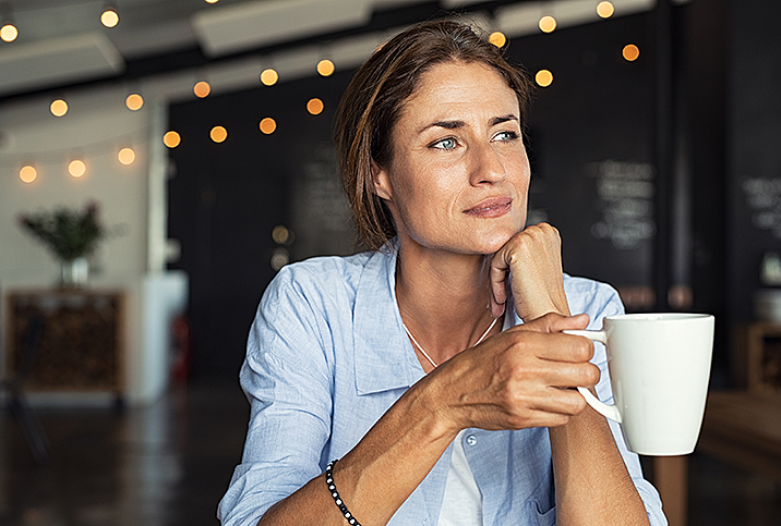 A woman holds a cup of tea and looks into the distance.