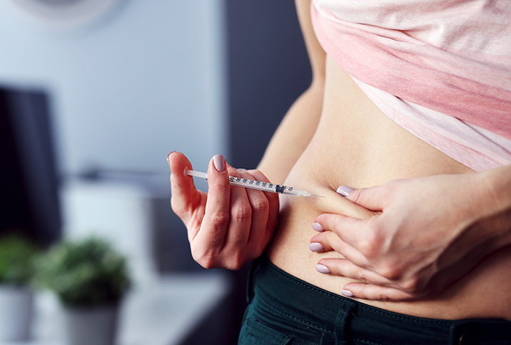 A woman pinches part of her stomach while administering an insulin injection.