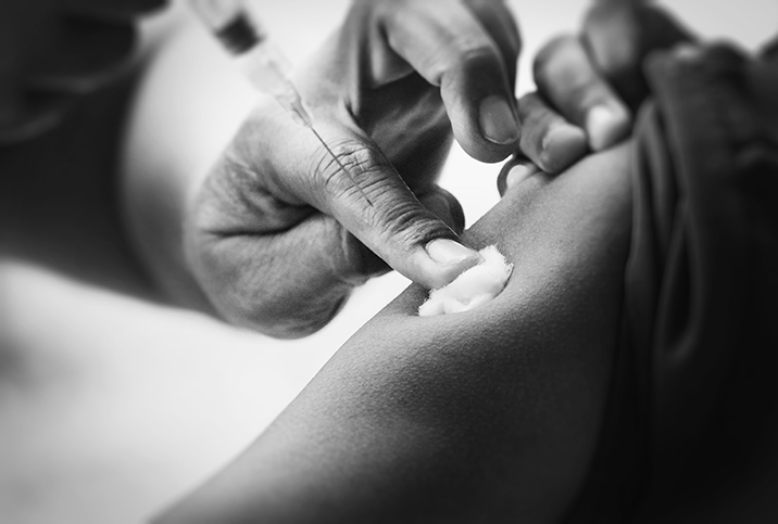 A finger holds a cotton ball to the spot on an arm of another person who has just received the meningitis vaccine.