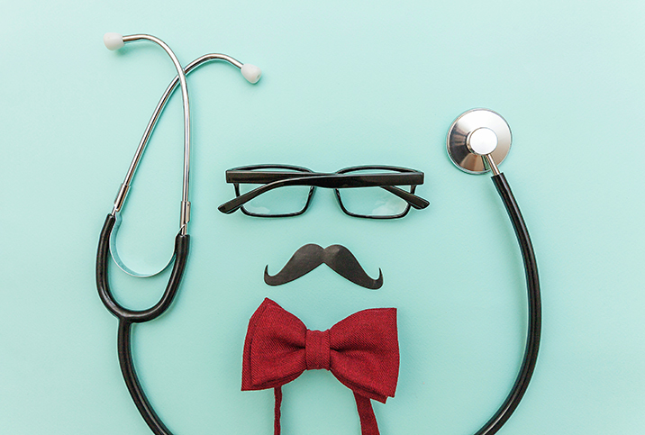 A pair of glasses and a mustache lay against a mint background with a bowtie beneath and surrounded by a stethoscope.
