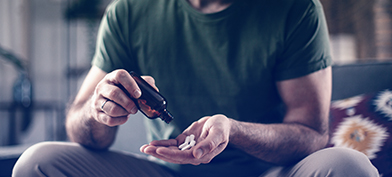 A man pours white pills from a brown bottle into his hand while sitting down.