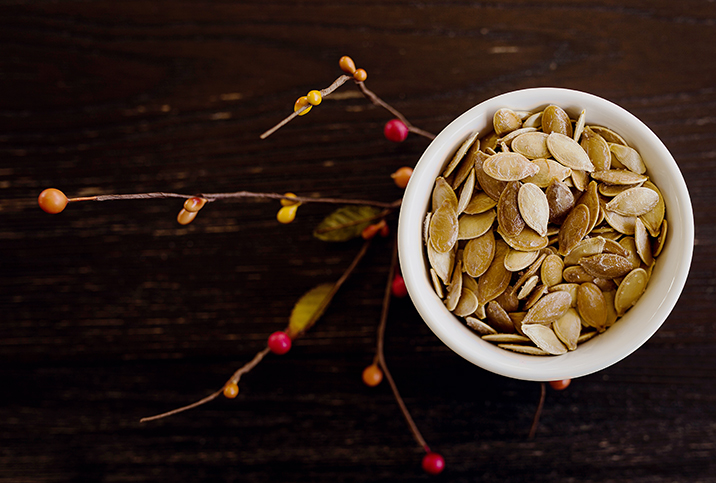A small bowl of pumpkin seeds sits on top of a branch growing red and yellow berries.