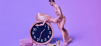 A Ken doll and a Barbie doll are in a sex position against an alarm clock with their pelvises pixelated.