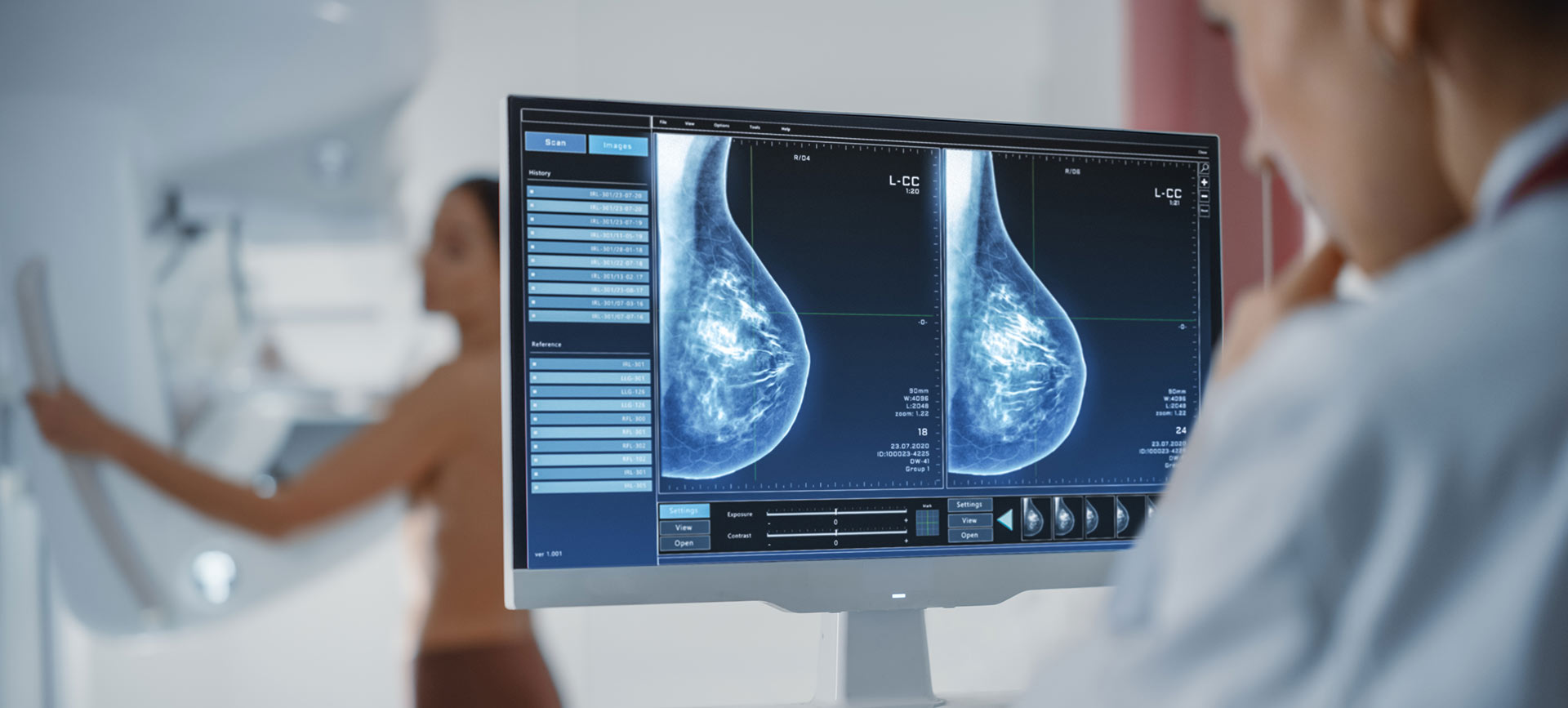 A doctor looks at a screen that shows a woman's mammogram who is standing in the background.