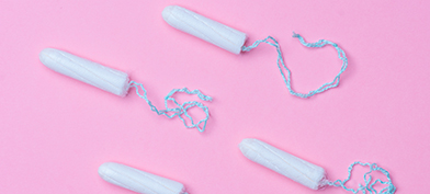 Four tampons without applicators lay against a pink surface.