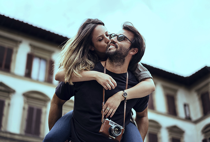 A man is giving a piggyback ride to a woman who is kissing his cheek.