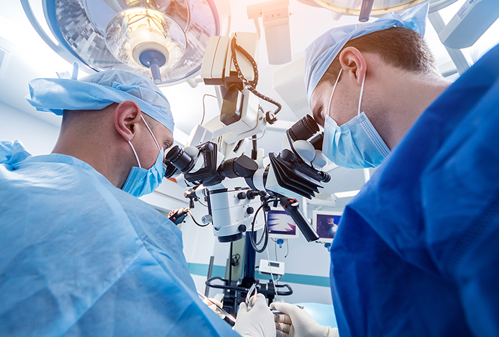 Two doctors look into a microsurgical machine during surgery.