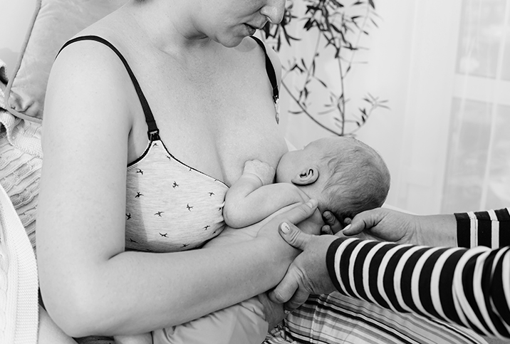 A lactation consultant adjusts a baby that is nursing from its parent's breast.