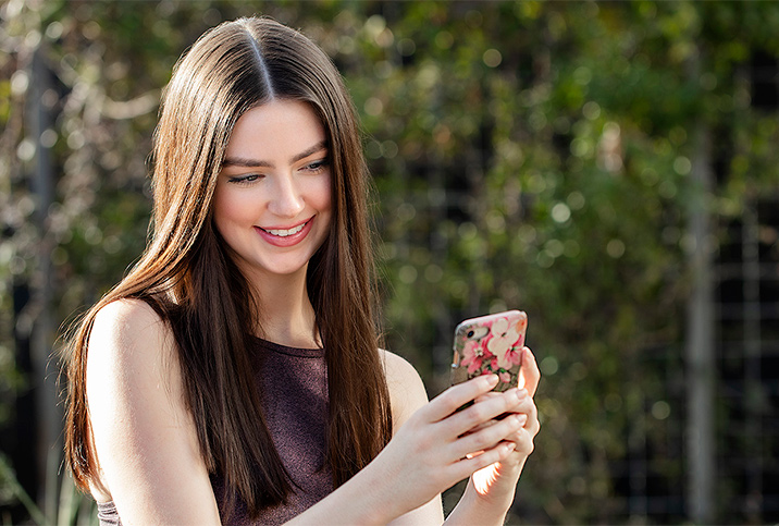 A woman looks at her phone smiling while taking a selfie.