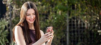 A woman looks at her phone smiling while taking a selfie.