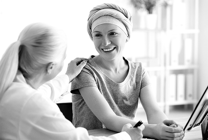 A woman with a headwrap smiles at another woman who touches her shoulder.