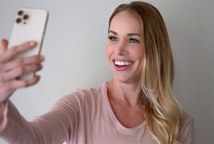 A woman smiles at her cellphone as she takes a selfie.