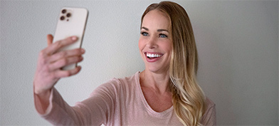 A woman smiles at her cellphone as she takes a selfie.