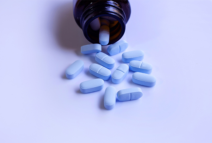 Blue pills spill out of a brown bottle onto a light blue surface.