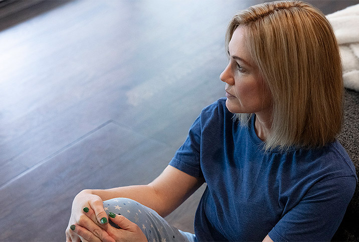 A woman sits on the wooden floor and looks into the distance.