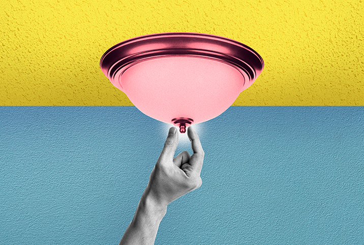 A black and white hand reaches up to pinch the tip of a pink light fixture that is on a yellow ceiling in front of a blue background.