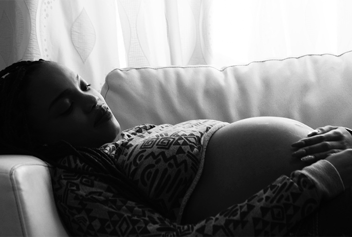 A pregnant person lies on on a couche and looks down at their pregnant belly.