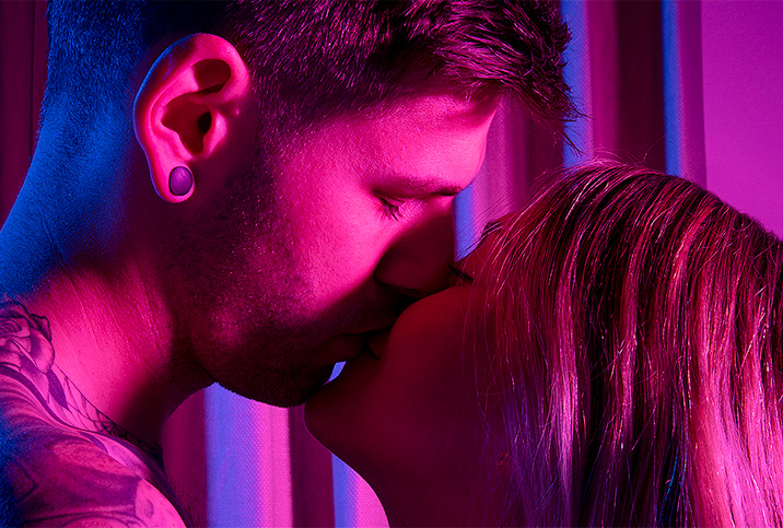 A man and woman kiss as a pink light shines on them.