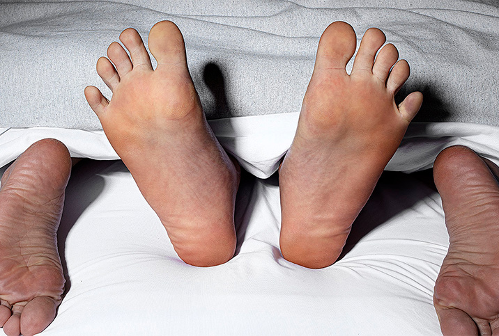 Two pairs of feet peek out from under white sheets in bed.