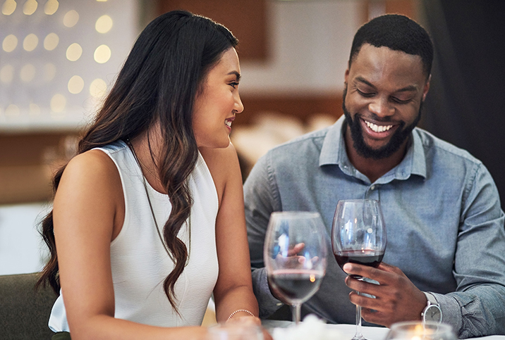 A man and woman are smiling as they talk and drink wine on a date.