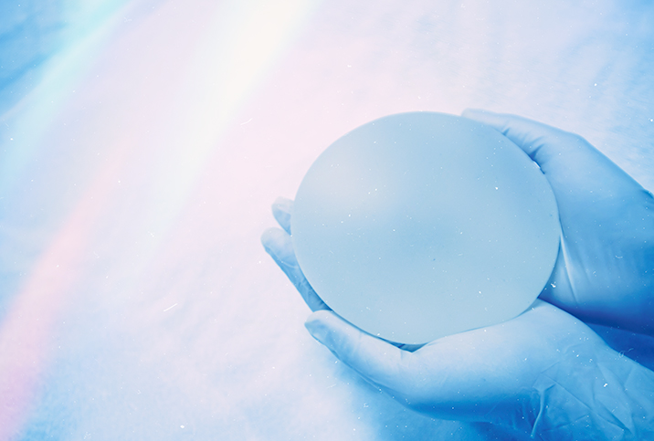 Two gloved hands hold a breast implant in their palms.