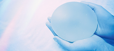 Two gloved hands hold a breast implant in their palms.