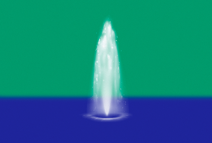 A fountain shoots water upwards in the middle of blue water against a green background.