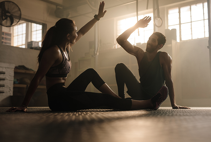 A man and a woman high-five while sitting down after a workout.