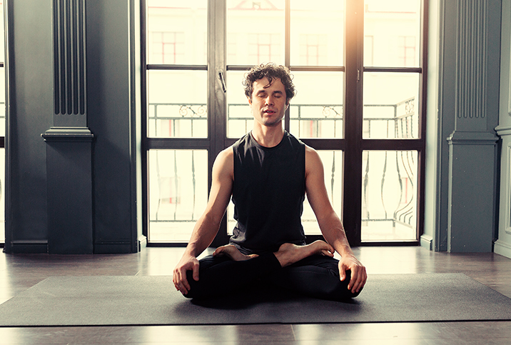 A man sits cross legged on a yoga mat with his eyes closed in meditation.