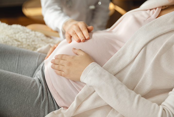 A pregnant woman holds her belly in two places while another person presses on it from the top.