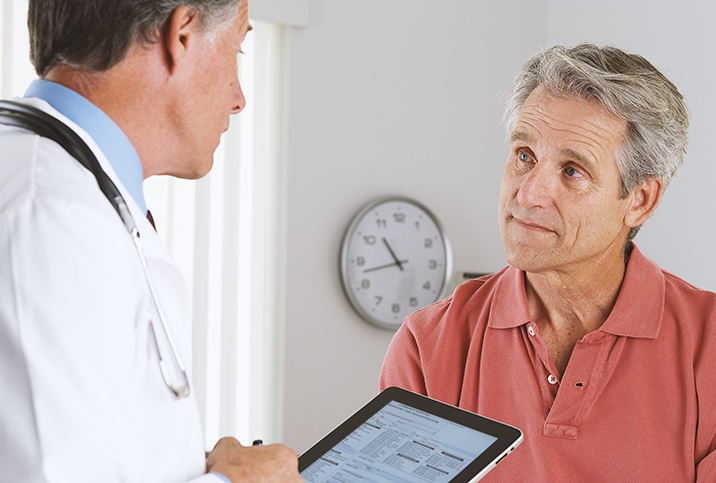 A male patient sits in front of a doctor with a tablet during a health screening.