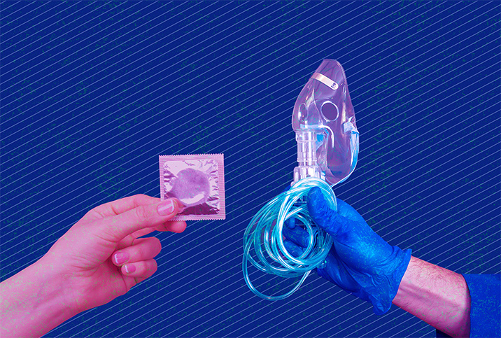 One hand holds a condom out towards another hand covered in a blue glove holding a breathing mask and tube.