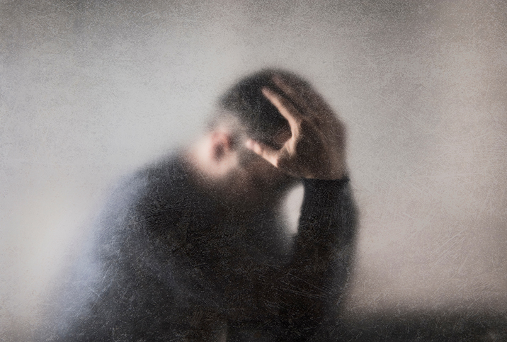 A man on the other side of a fogged glass, holds his head in his hands.