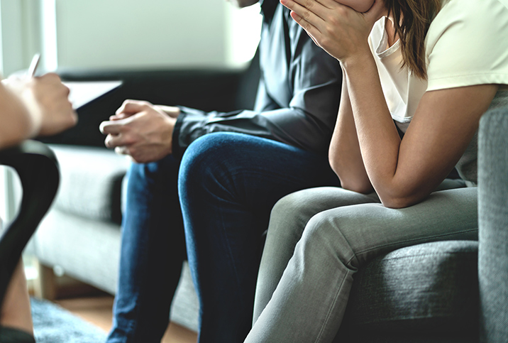 A woman sits next to a man on a couch with her hand in her hands.