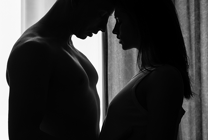 A man and a woman stand facing each other with their foreheads pressed together in the dark.