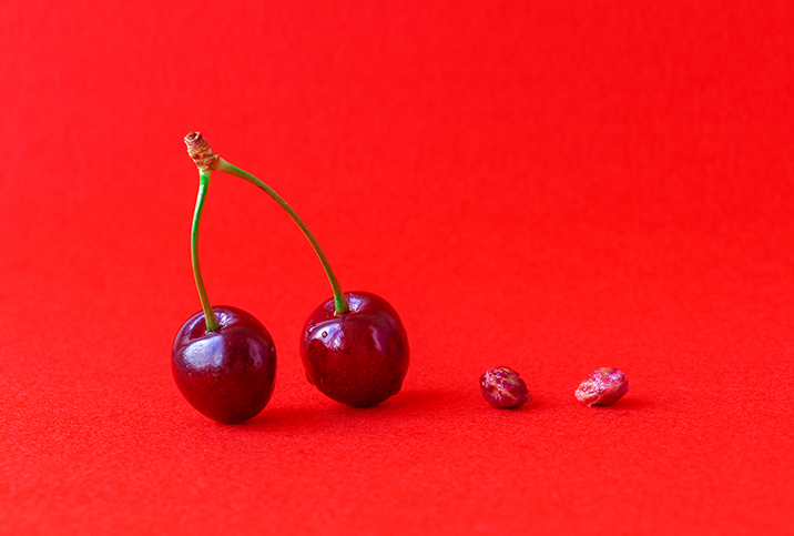 A pair of cherries on stems is on the left and a pair of cherry pits is on the right.