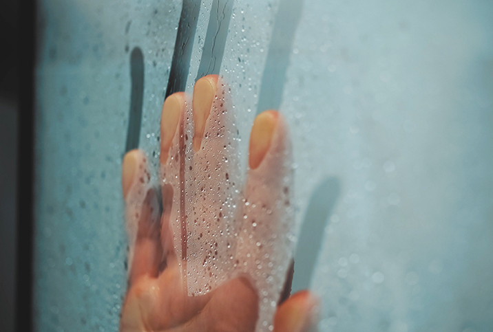 A hand streaks down a fogged up window covered in condensation.