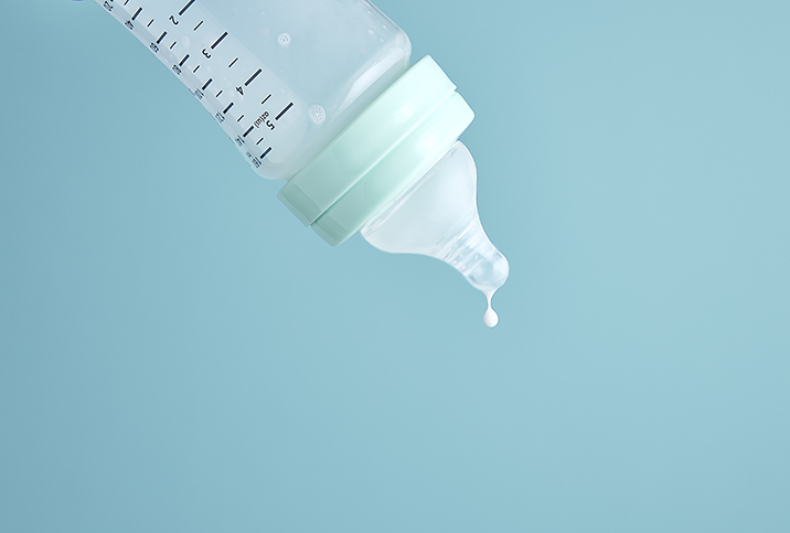 An empty formula bottle tips downward with a single drop of milk falling from the nipple.